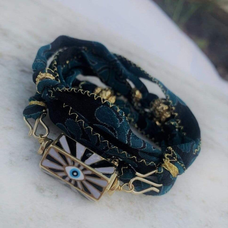 Cordon en soie de sari marine et turquoise présenté en bracelet 5 tours, customisé d'un pendentif mauvais oeil gris et noir